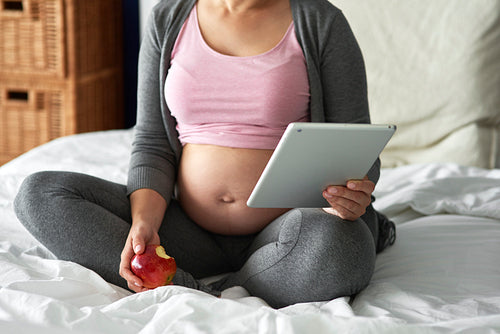 Unrecognizable pregnant woman using tablet while sitting in bed