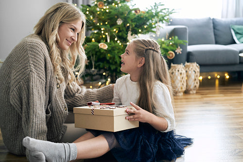 Caucasian girl holding her dreamy Christmas gift and mother cheerful mother next to her