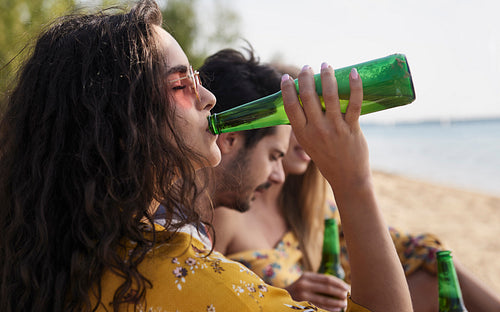 Close up of girl drinking beer with friends on the beach.