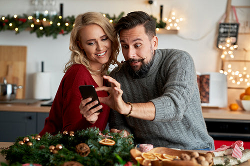 Couple with a Christmas wreath using a mobile phone