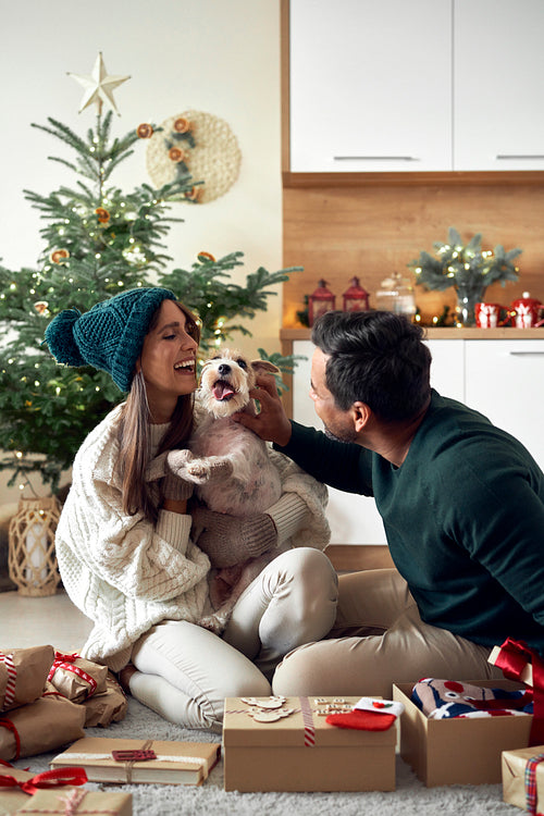 Happy couple opening Christmas presents with dog at home