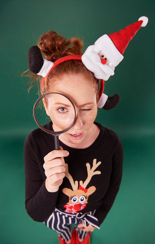 Woman in christmas clothes looking through magnifying glass