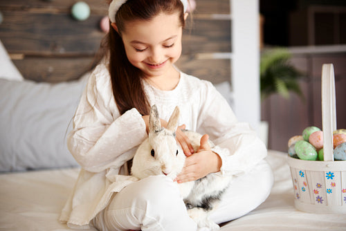 Cute girl stroking fluffy rabbit in bed