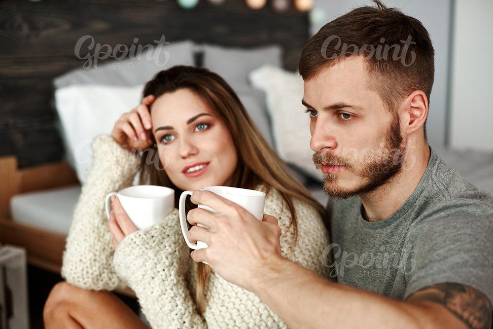 Couple with coffee sitting on floor at bedroom