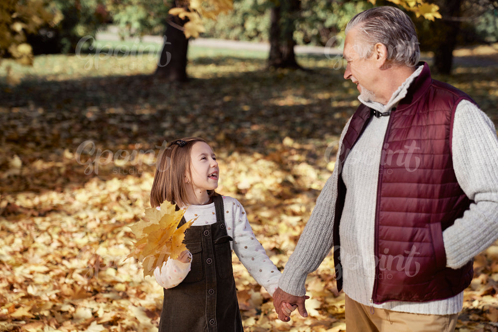 Little girl spending time with grandfather at the park in autumn 