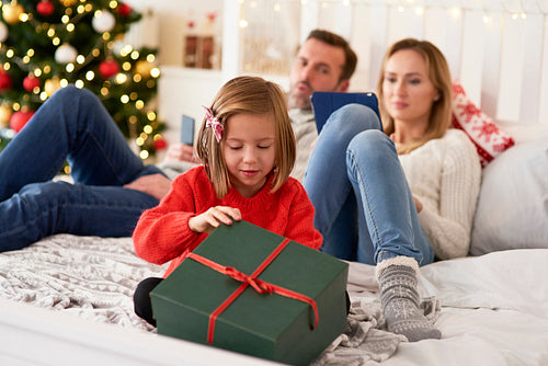 Child opening  gift and parents with technology in the background