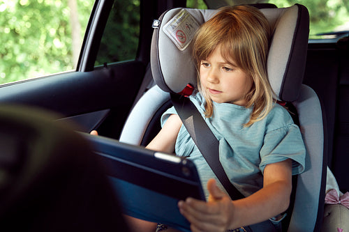 Little girl on rear seat of car with tablet