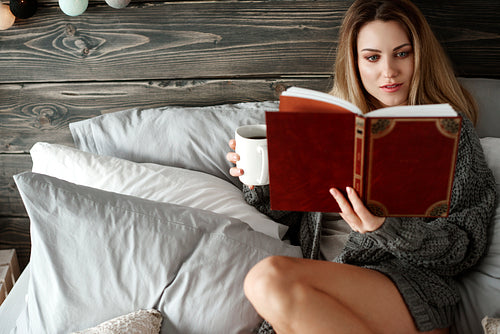 Interested woman with morning coffee reading a book at bedrooom