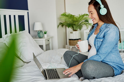 Cheerful pregnant woman listening music from the laptop