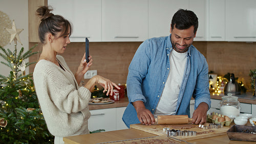 Close up of multi ethnicity couple making a gingerbreads and using mobile phone in Christmas time.