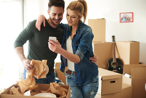Cheerful couple using phone while moving house