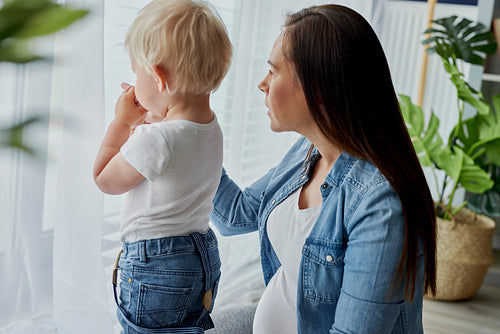 Woman and her toddler son standing next to the window