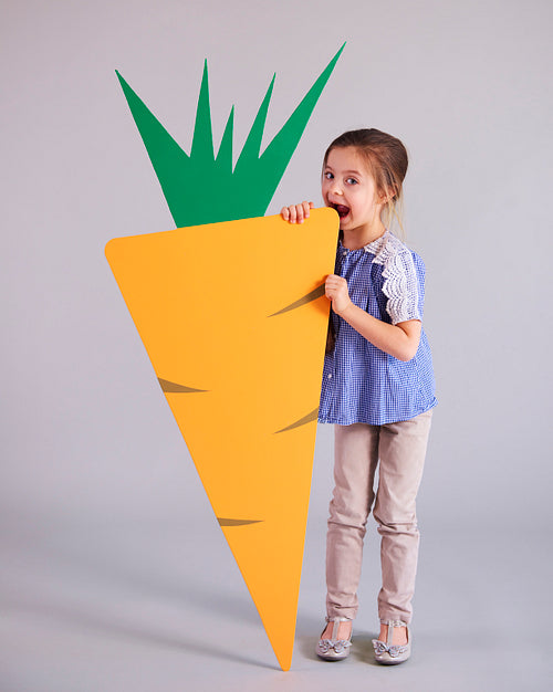 Playful girl eating a huge, artificial carrot