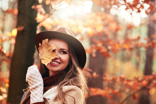 Happy beautiful woman  covering eye with autumnal leaves