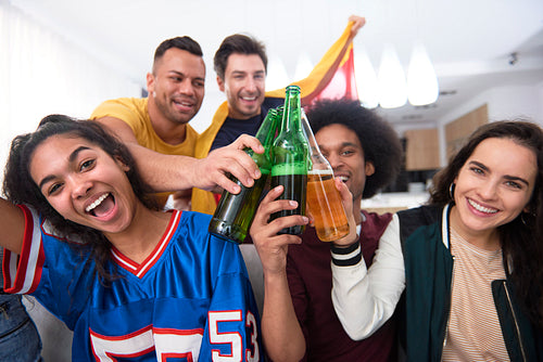 Group of smiling friends toasting with beer bottle at home