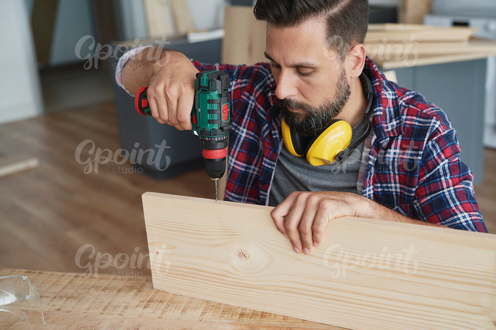 Focused carpenter drilling in a wooden plank
