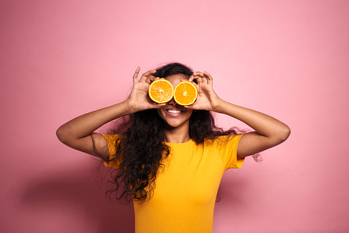 African woman covering her eyes with oranges in studio shot.