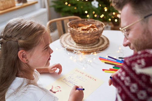 Writing letter to Santa Claus by cute little girl with daddy
