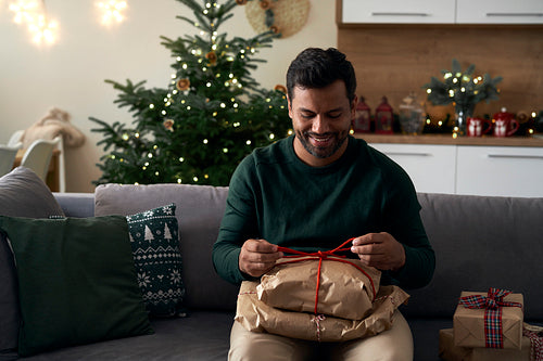 Latino man with Christmas present sitting on sofa at home