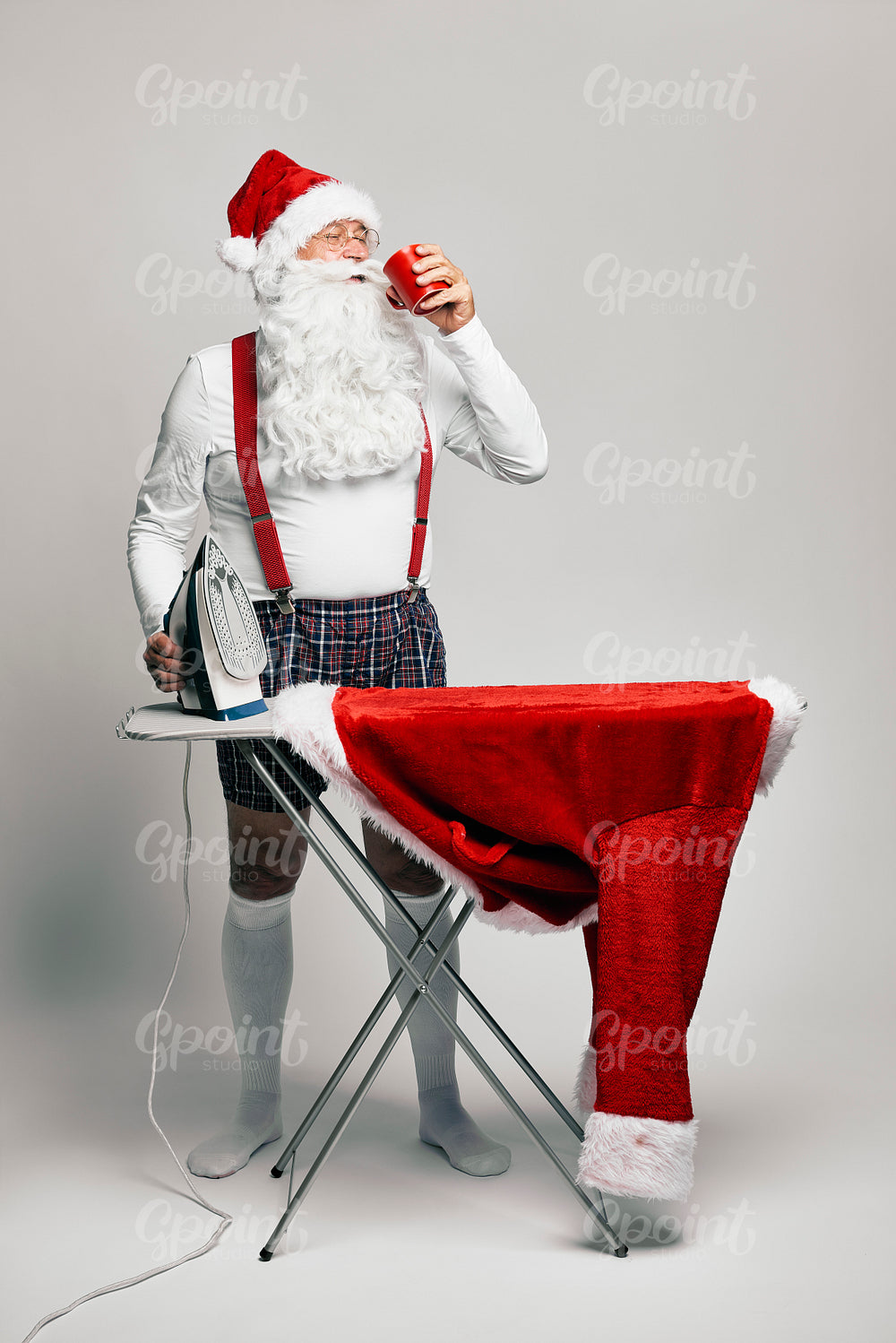 Caucasian Santa Claus ironing trousers for Christmas and drinking hot chocolate 