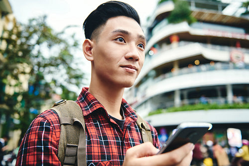 Asian man holding mobile phone and looking away