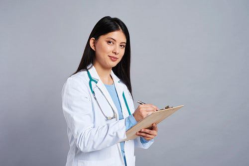 Female Asian doctor making some notes in clipboard