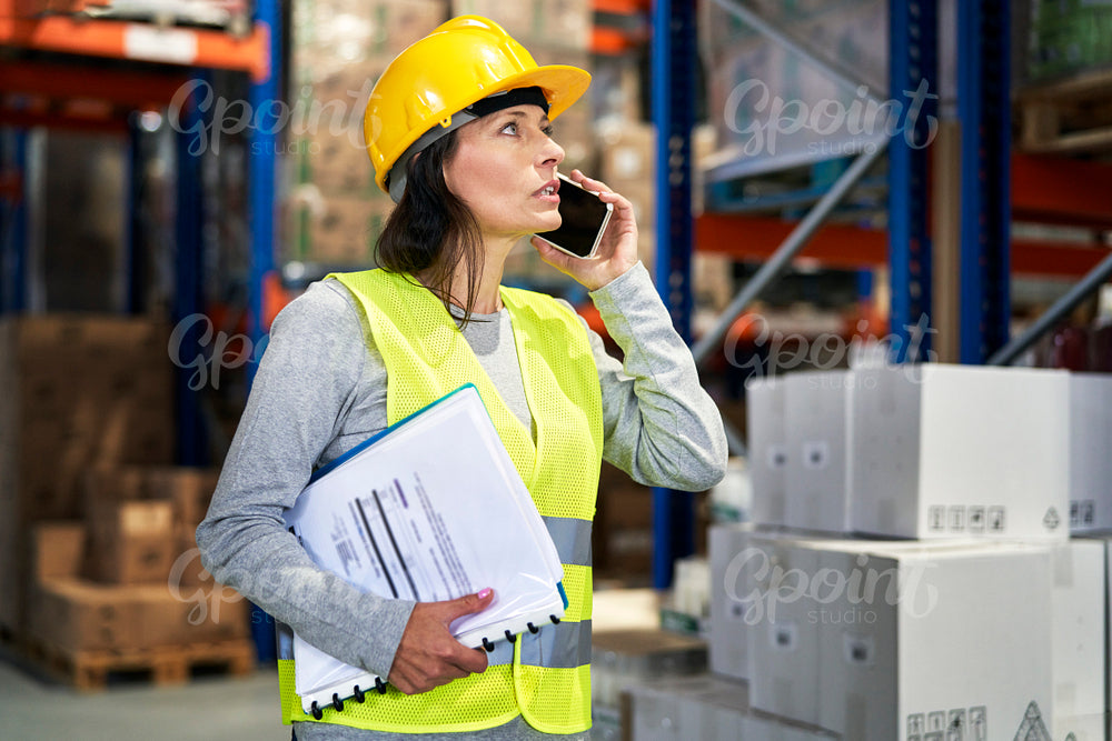 Adult caucasian woman talking on the mobile phone and looking up in warehouse 