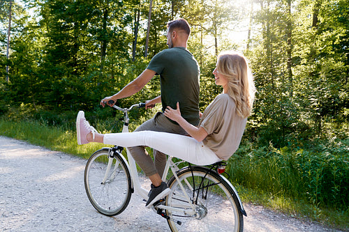Rear view of couple sharing a bicycle in the forest