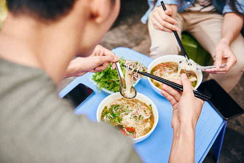 Close up of couple eating pho soup in the city