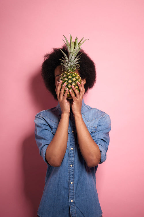 African man with pineapple covering face in a studio shot.