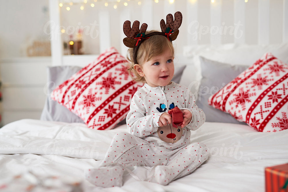 Charming baby opening the Christmas present in bed