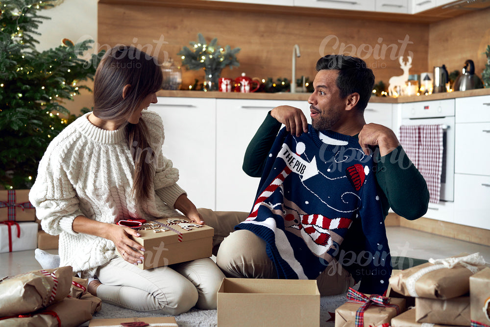 Multi ethnicity couple opening Christmas presents at home