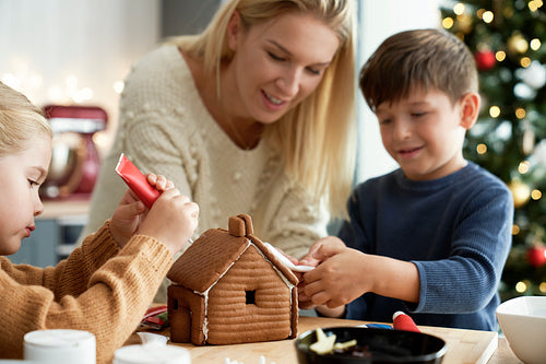 Happy children decorating gingerbread house with their mom