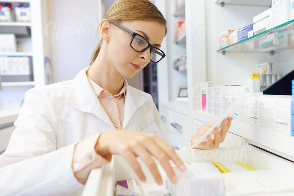 Female pharmacist browsing medicines on shelf