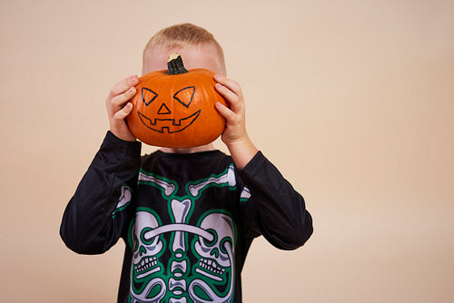 Little boy holding halloween pumpkin in front of his face