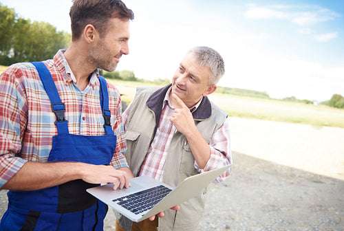 Thoughtful farmers talking over laptop