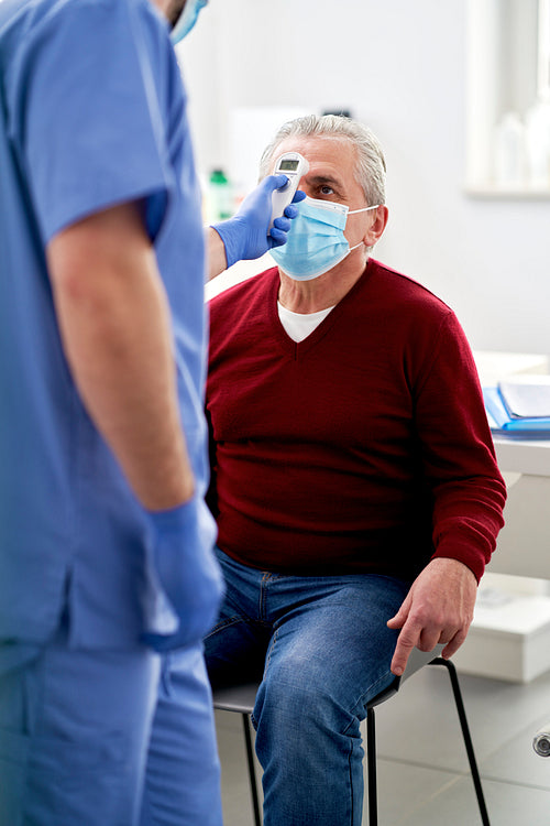 Senior patient in doctor's office while taking a temperature measurement