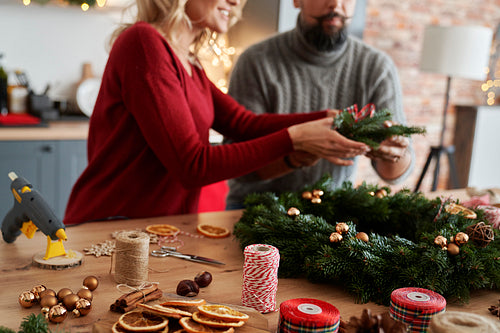 Couple making Christmas wreath at table full of decorations