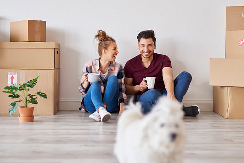 Cheerful couple with coffee cups relaxing in their new apartment