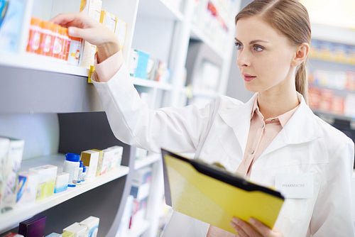 Young pharmacist looking at shelf of pills