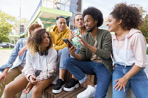 Group of young friends sitting and talking together with mobile phone