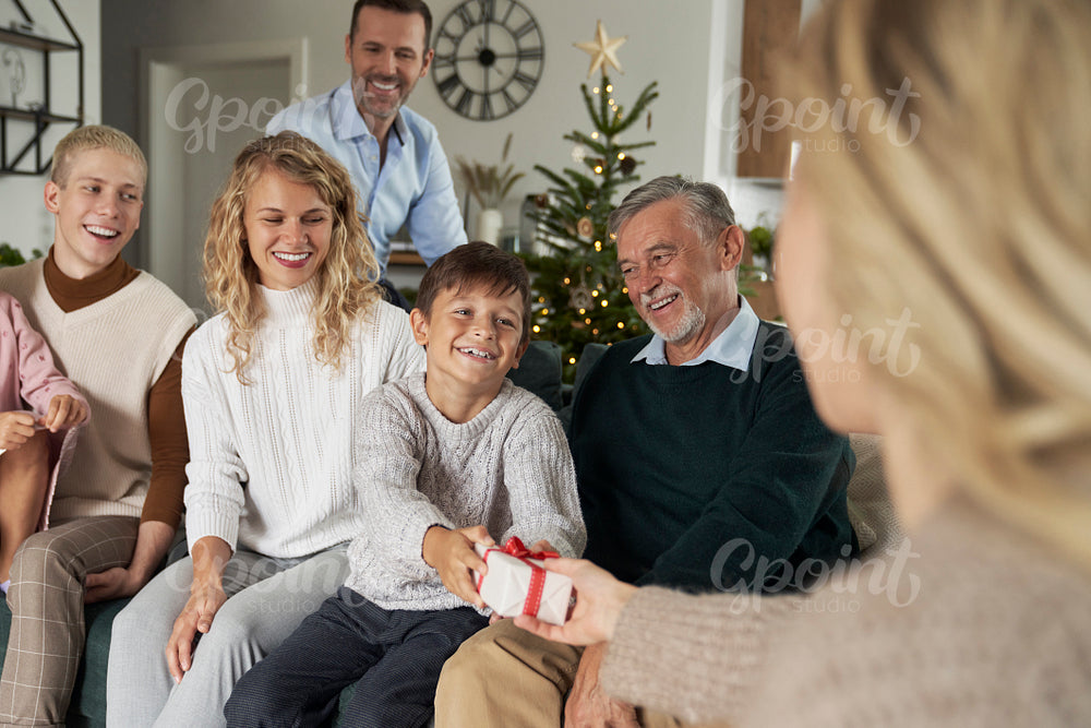 Caucasian boy giving Christmas present to his mom and family sitting around
