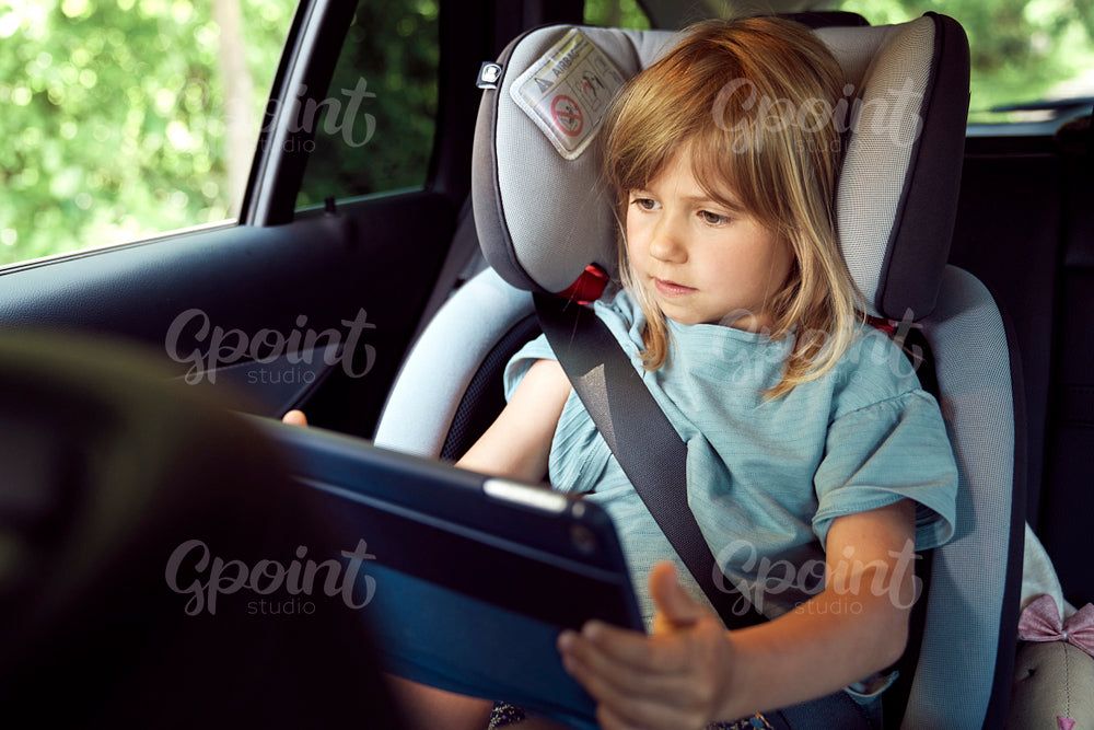 Little girl on rear seat of car with tablet