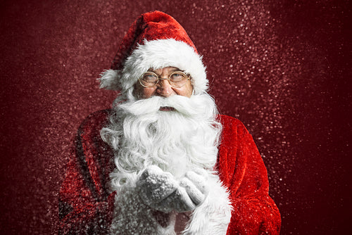 Close up of caucasian Santa Claus on red background blowing snow
