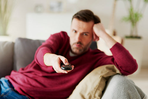 Bored man holding a remote and watching TV