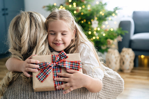 Caucasian little girl embracing mother and being grateful for her Christmas present