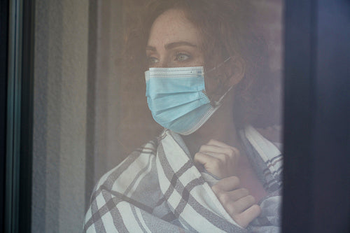 Caucasian red head woman with protective mask standing indoors next to the window