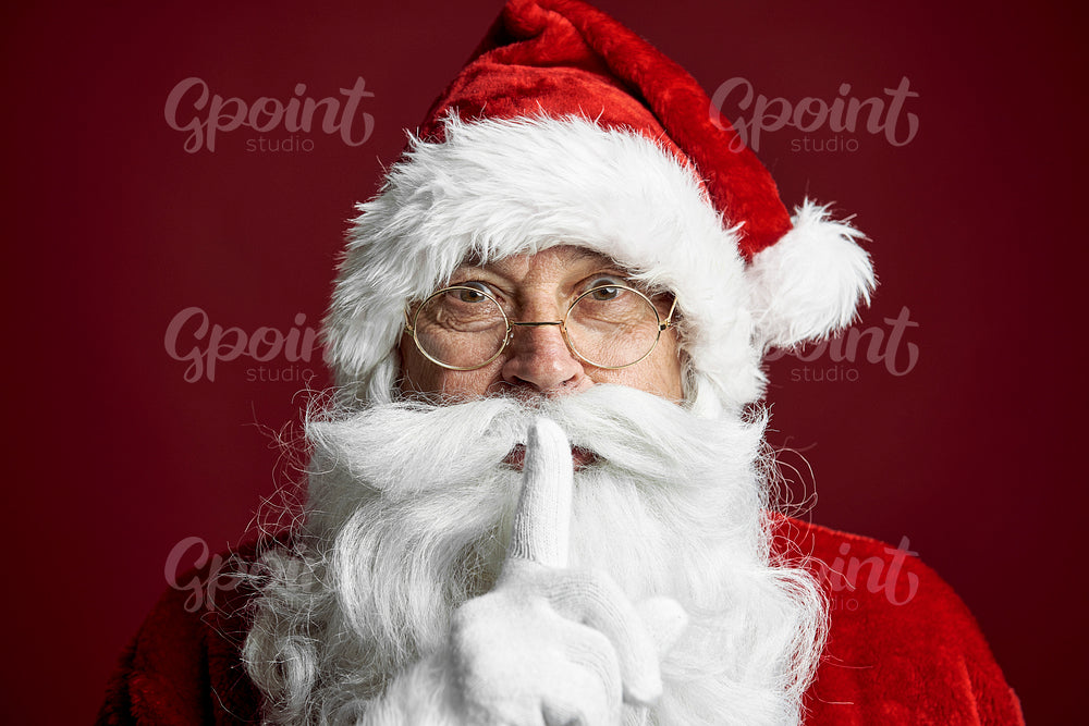 Santa Claus standing on the red background and showing quiet sign 
