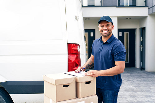 Portrait of courier standing with packages next to a delivery van
