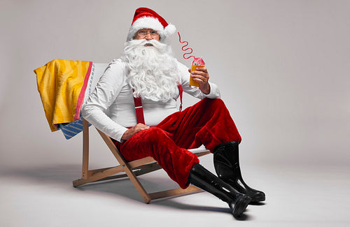 Caucasian Santa Claus with drink and sunbed on grey background